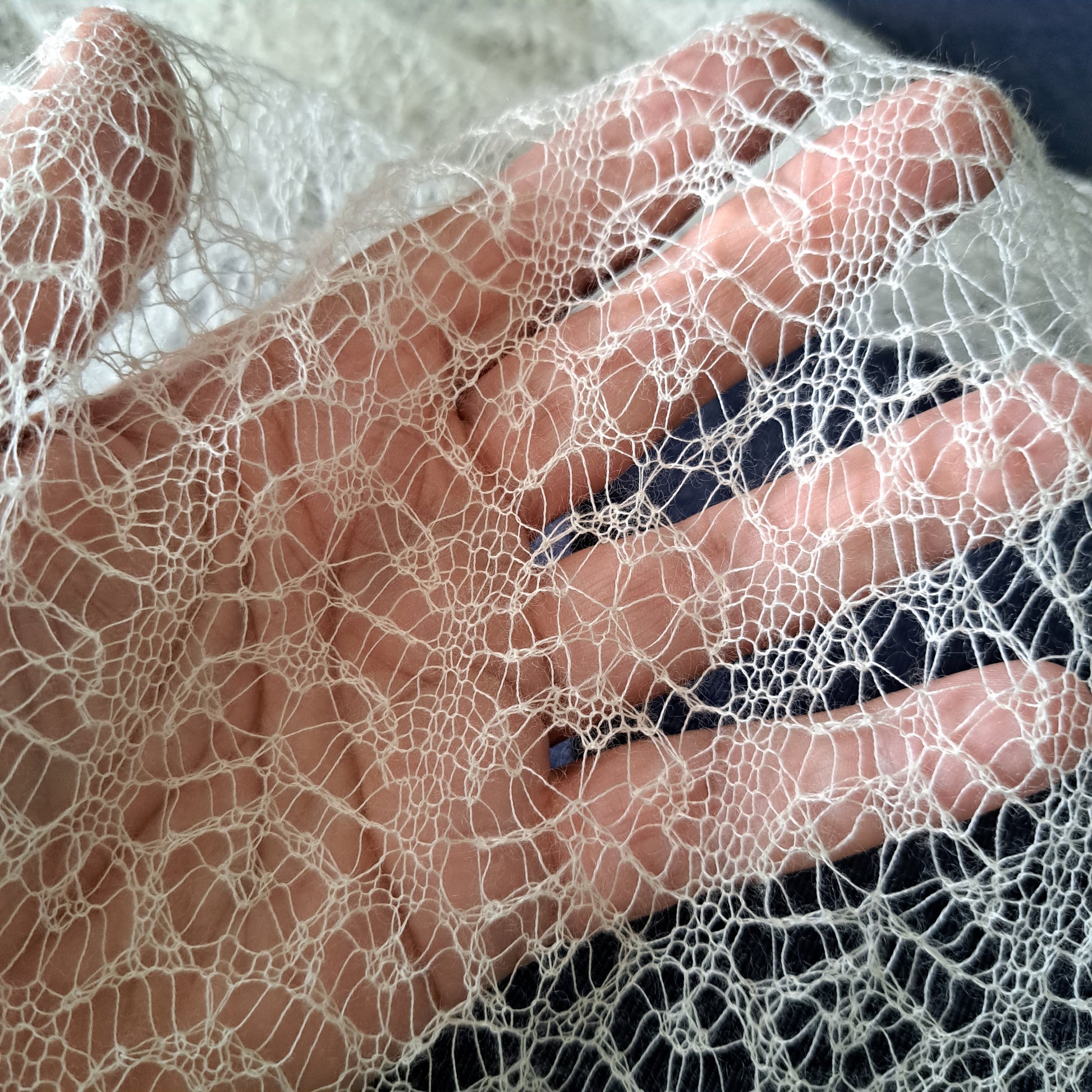 A white gossamer shawl, heavily patterned fine lace, held over a hand.